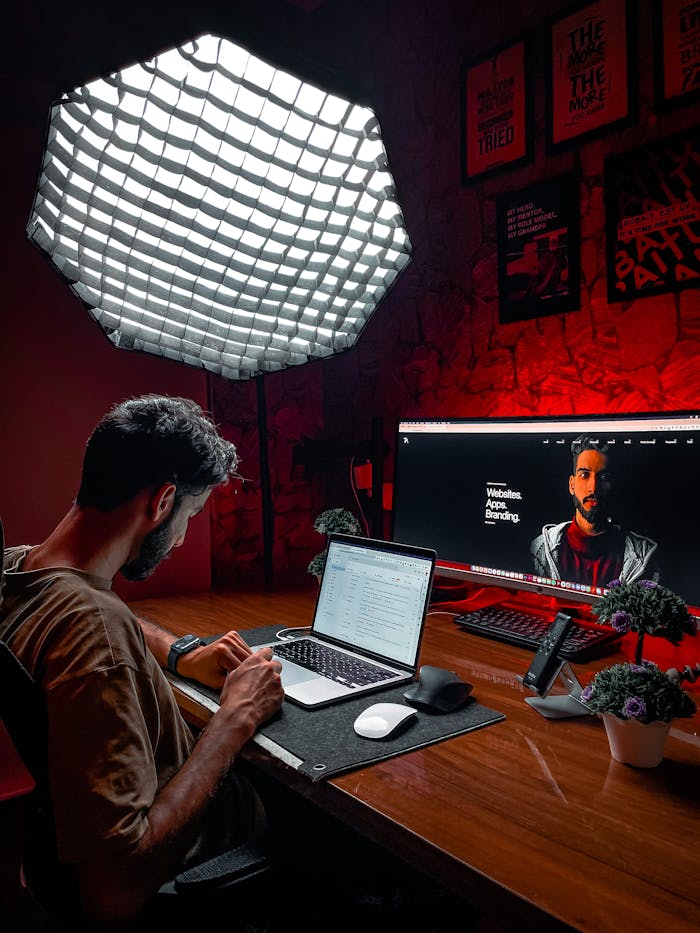 Asian man working at a laptop in a stylish red-lit room with modern equipment and lighting.